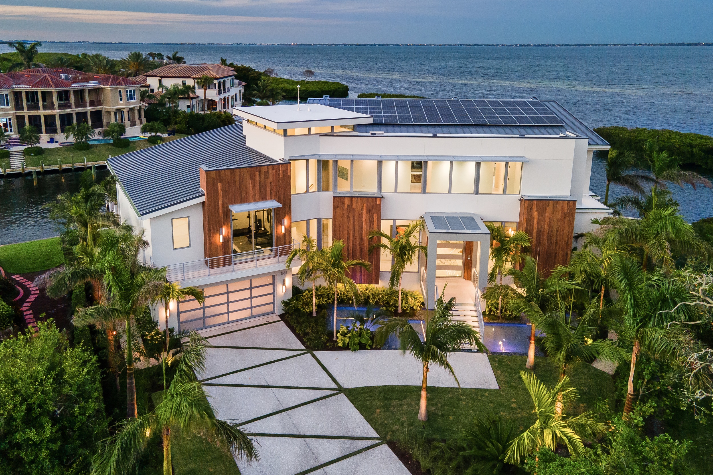 Luxury waterfront home with palm trees and solar panels.